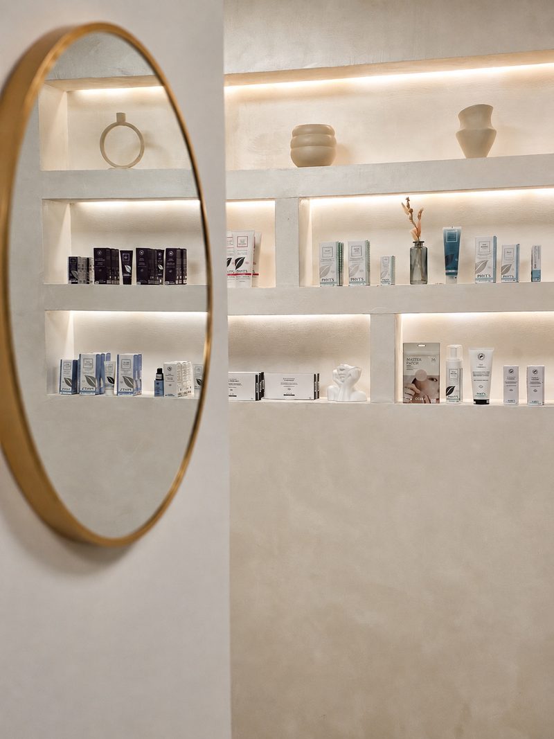 Étagères rétroéclairées garnies de cosmétiques et grand miroir rond doré, dans la boutique So Bodyful